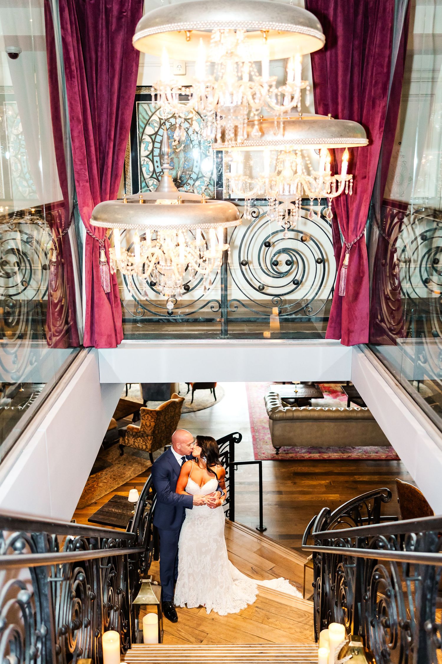 Elegant ballroom interior with crystal chandeliers, burgundy curtains, and ornate railings in warm lighting.