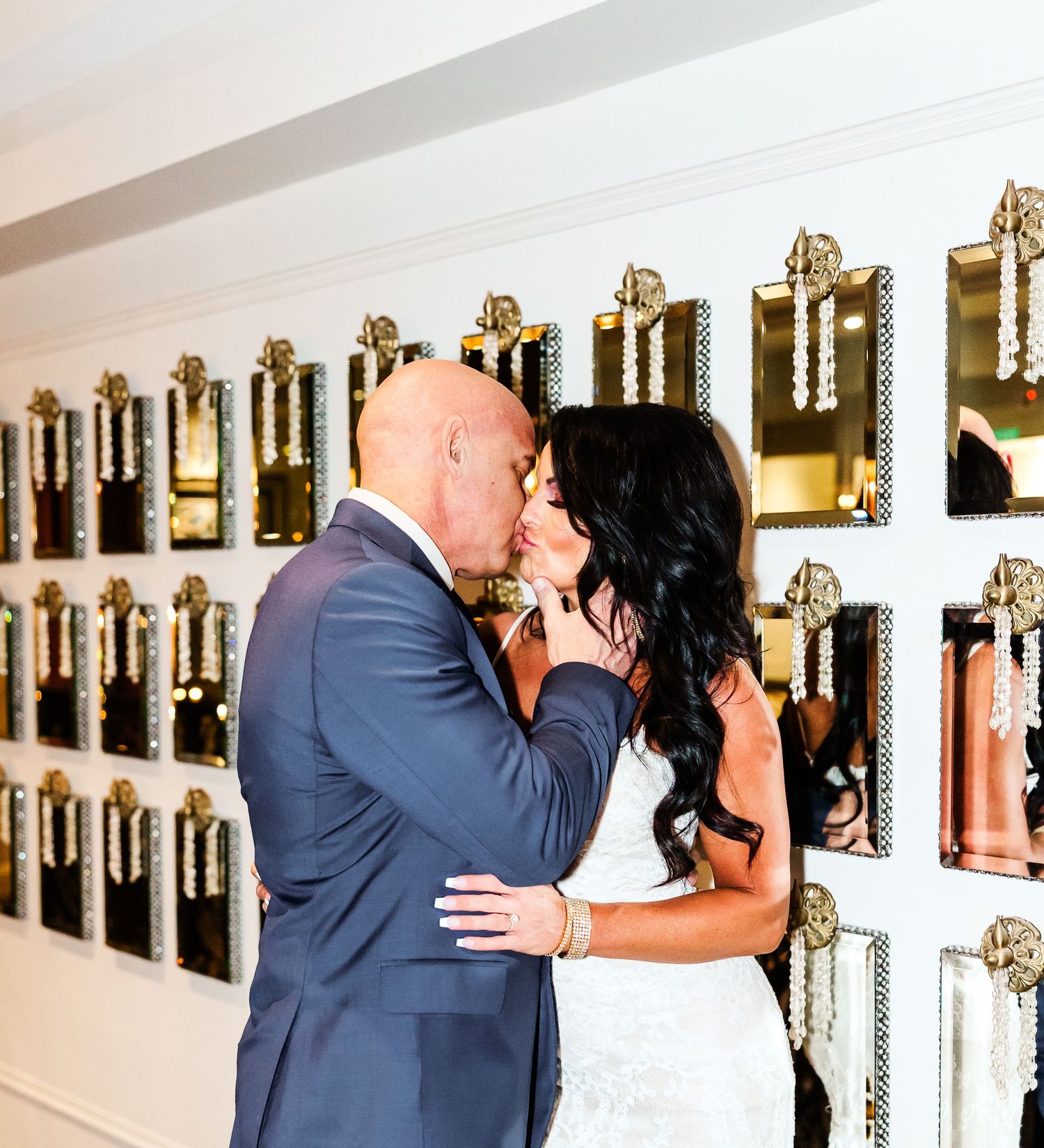 A couple in formal attire share an intimate moment in a hallway with framed photos on the wall.