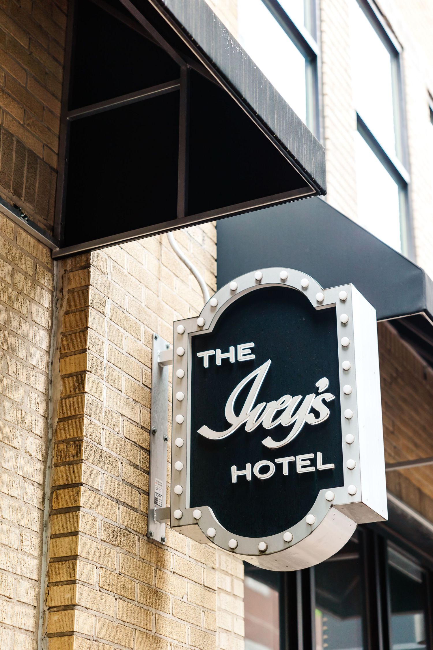 A black and white illuminated sign for The Ivy's Hotel mounted on a brick wall beneath a dark awning.