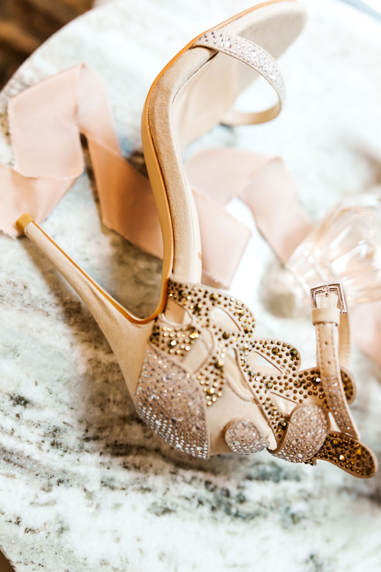 Elegant bridal shoes with sparkling crystal embellishments and delicate straps photographed on white textured surface.