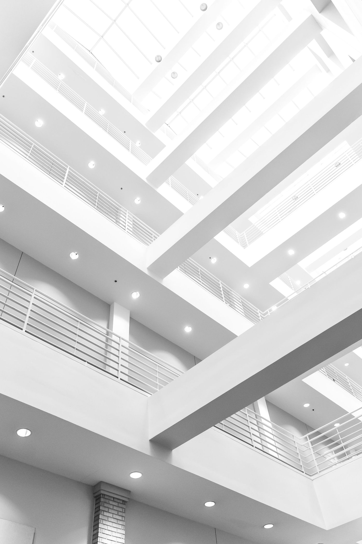 Modern architectural interior with white geometric skylights and multiple levels featuring minimalist railings and recessed lighting.