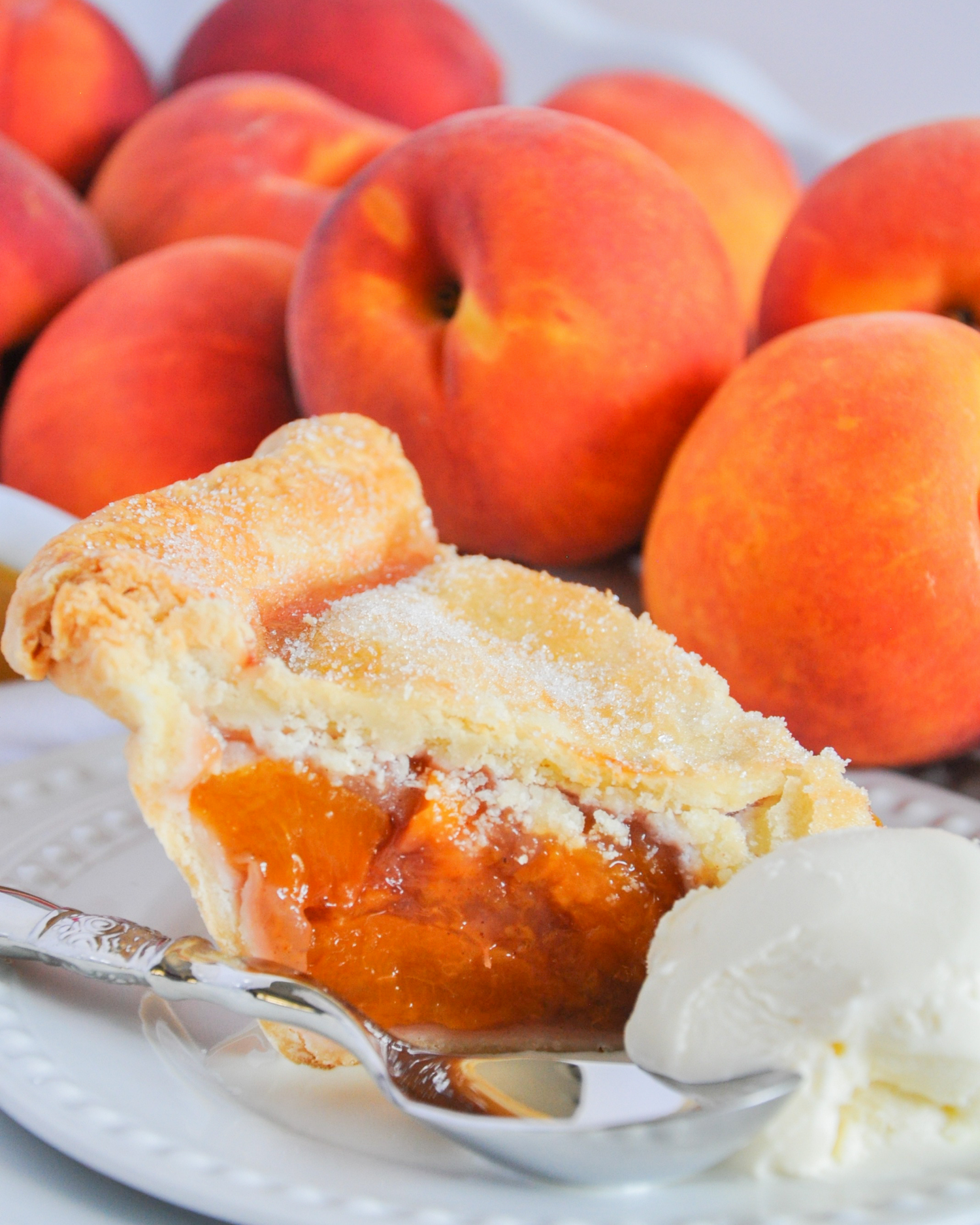 Fresh peaches and a slice of peach pie with vanilla ice cream on a white plate.