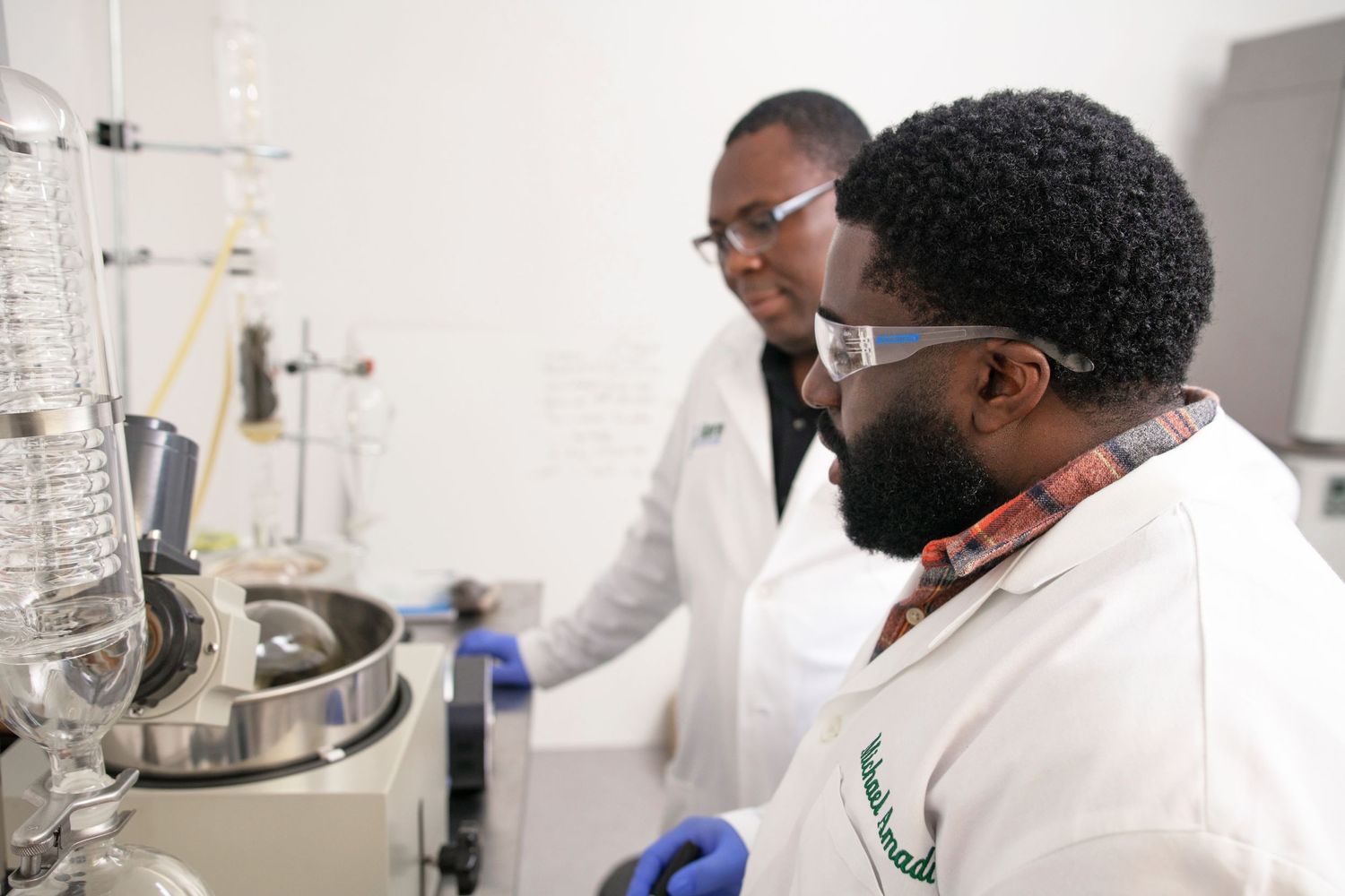 Two scientists in white lab coats work together analyzing laboratory equipment in a research facility.