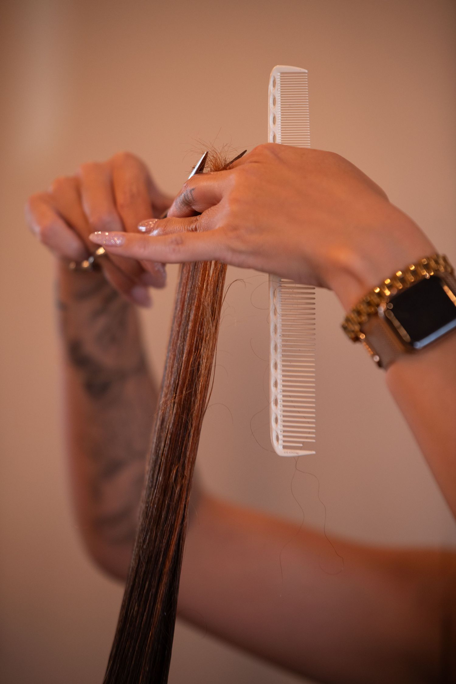 Close-up of hands using scissors and comb to cut long straight hair at a salon.