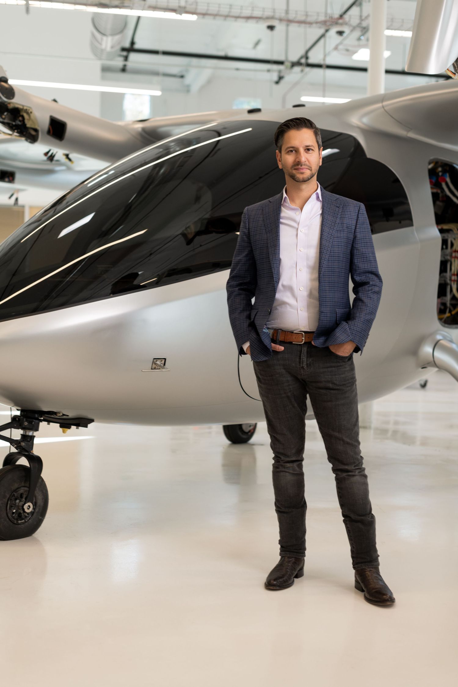 Professional in business attire stands next to a sleek private aircraft in a bright hangar interior.