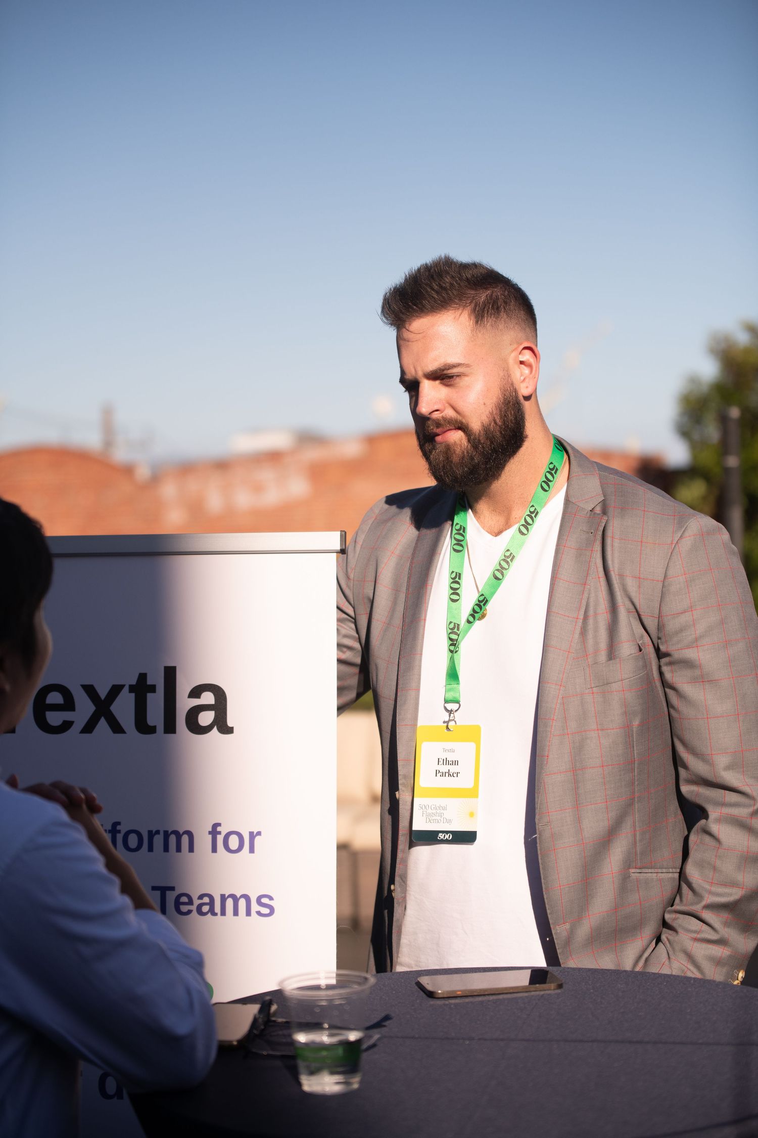 A bearded professional wearing a badge and gray blazer stands at a conference booth with Extla branding in the background.