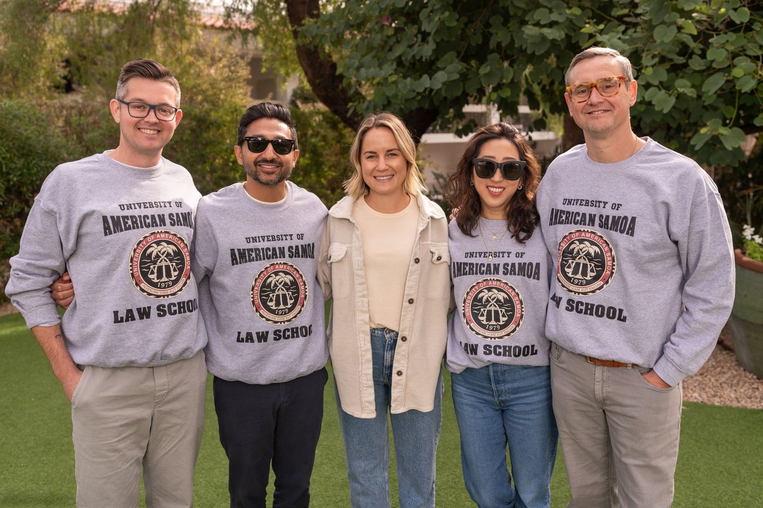 Five people in matching University of Cincinnati Law School sweatshirts stand together outdoors on a sunny day.