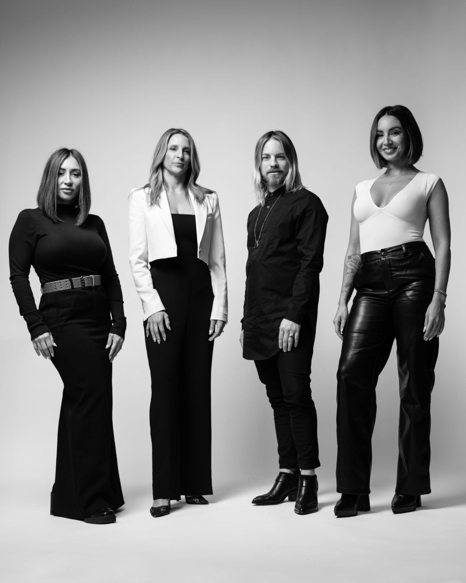 A black and white professional portrait of four musicians posed together against a white background.