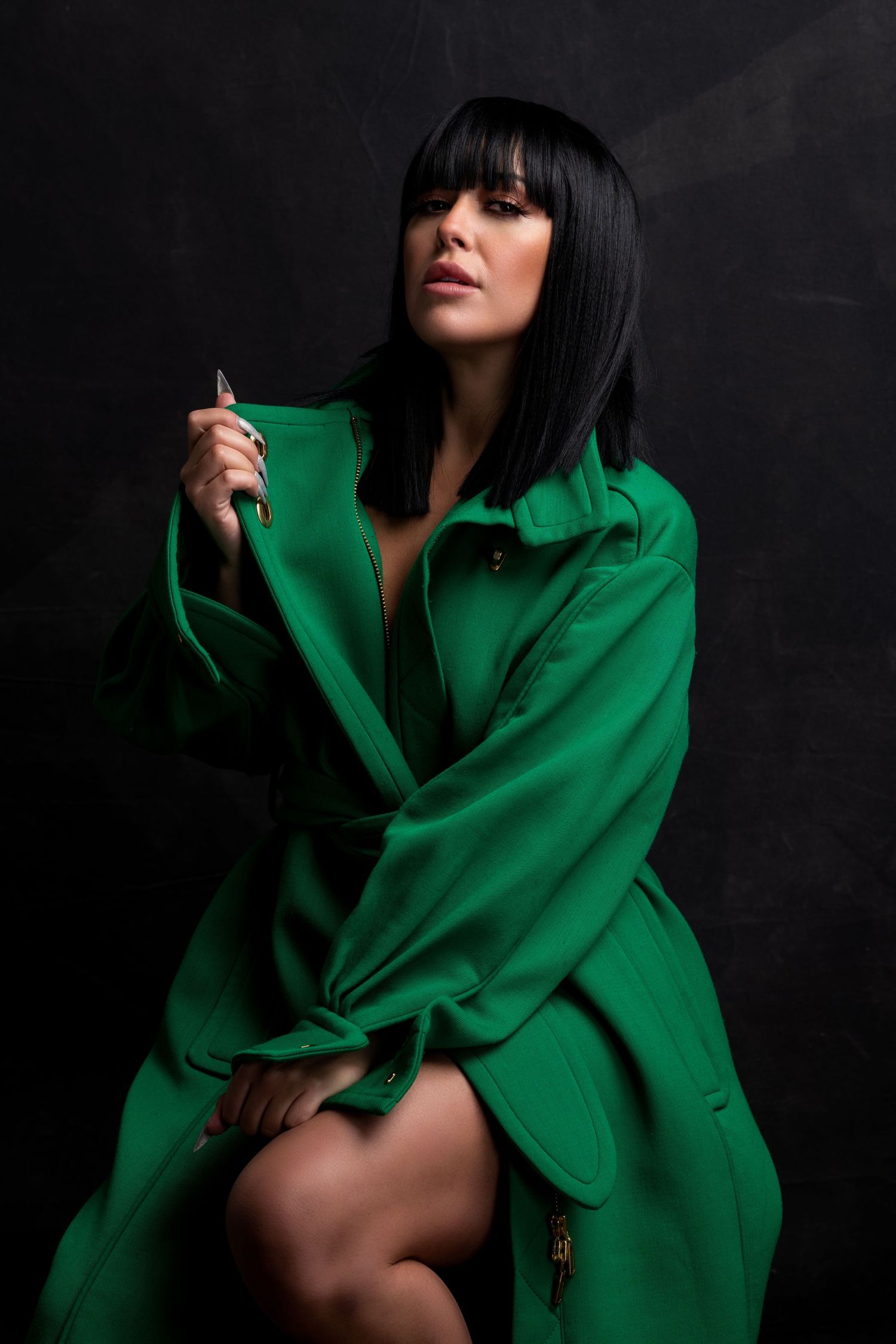 Fashion portrait with emerald green trench coat against dark background in dramatic studio lighting.