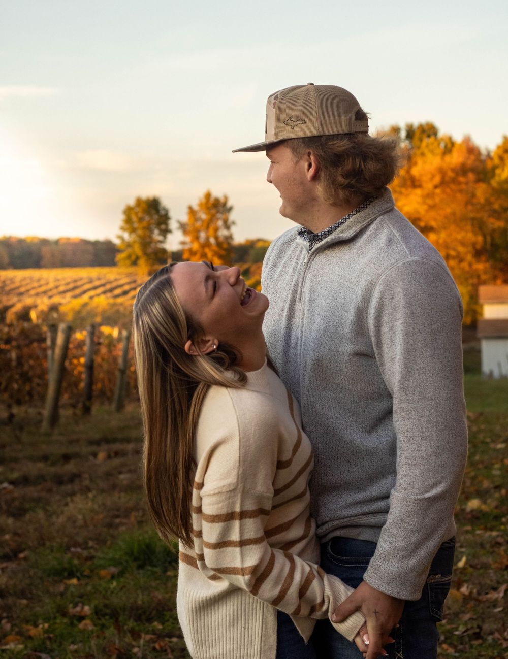 A couple embraces while walking through a vineyard during golden autumn sunset.