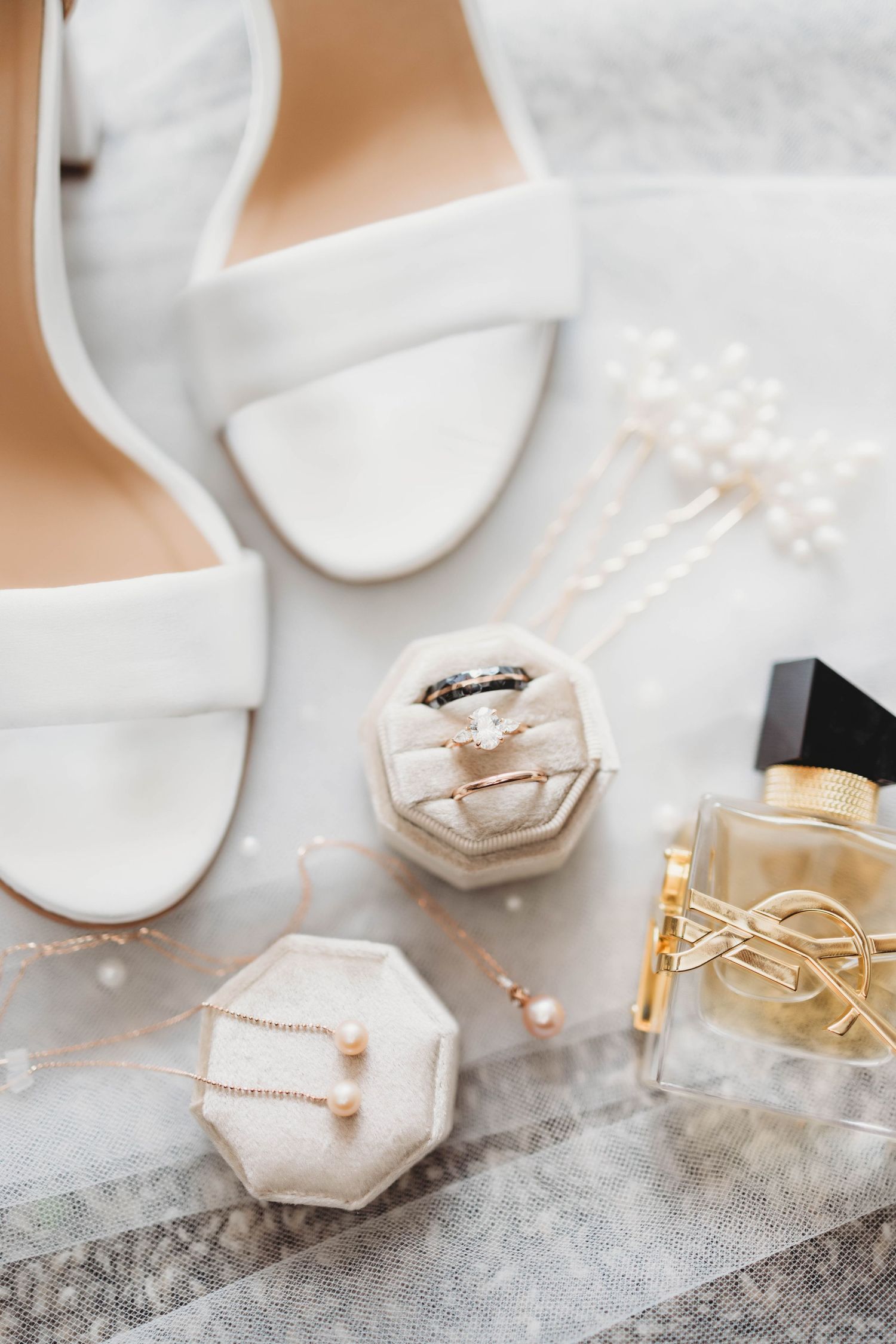 Wedding accessories and jewelry arranged on a light colored surface with geometric ring boxes.