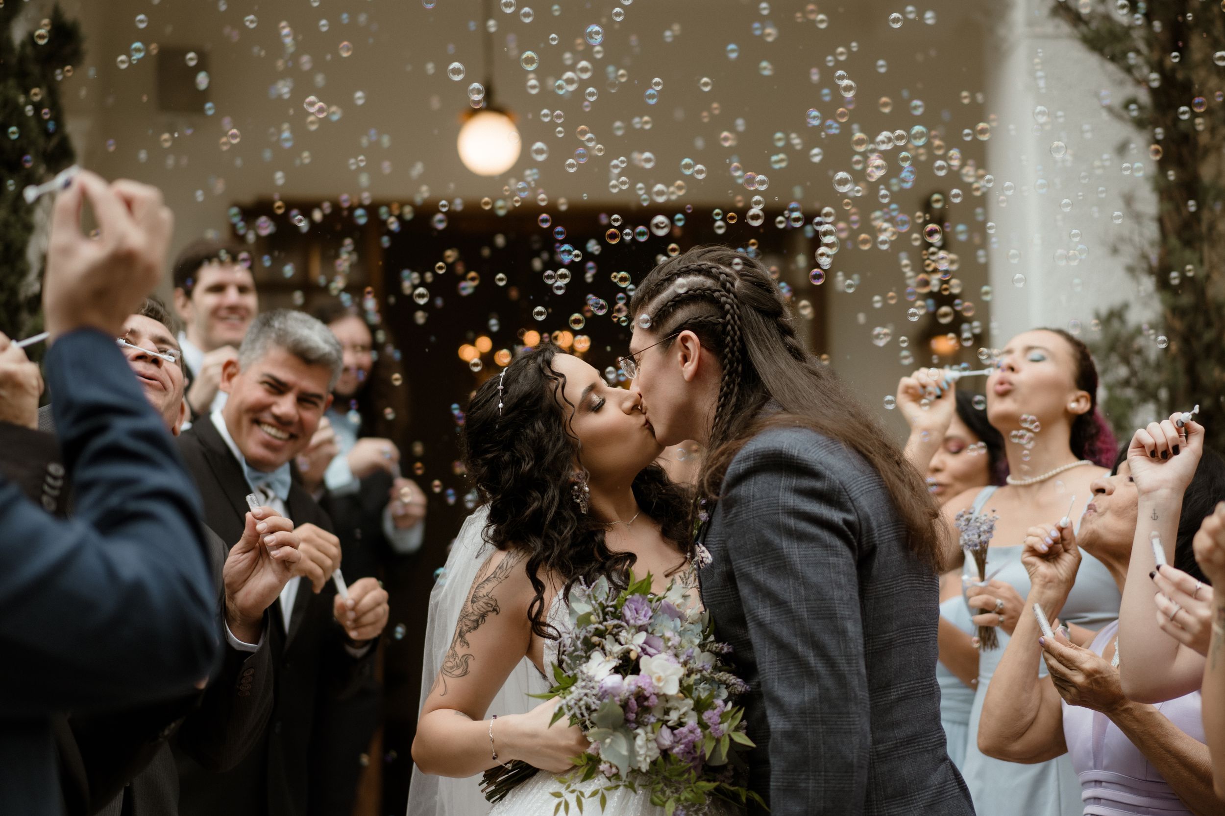 Couple shares joyful moment surrounded by bubbles and celebrating wedding guests.