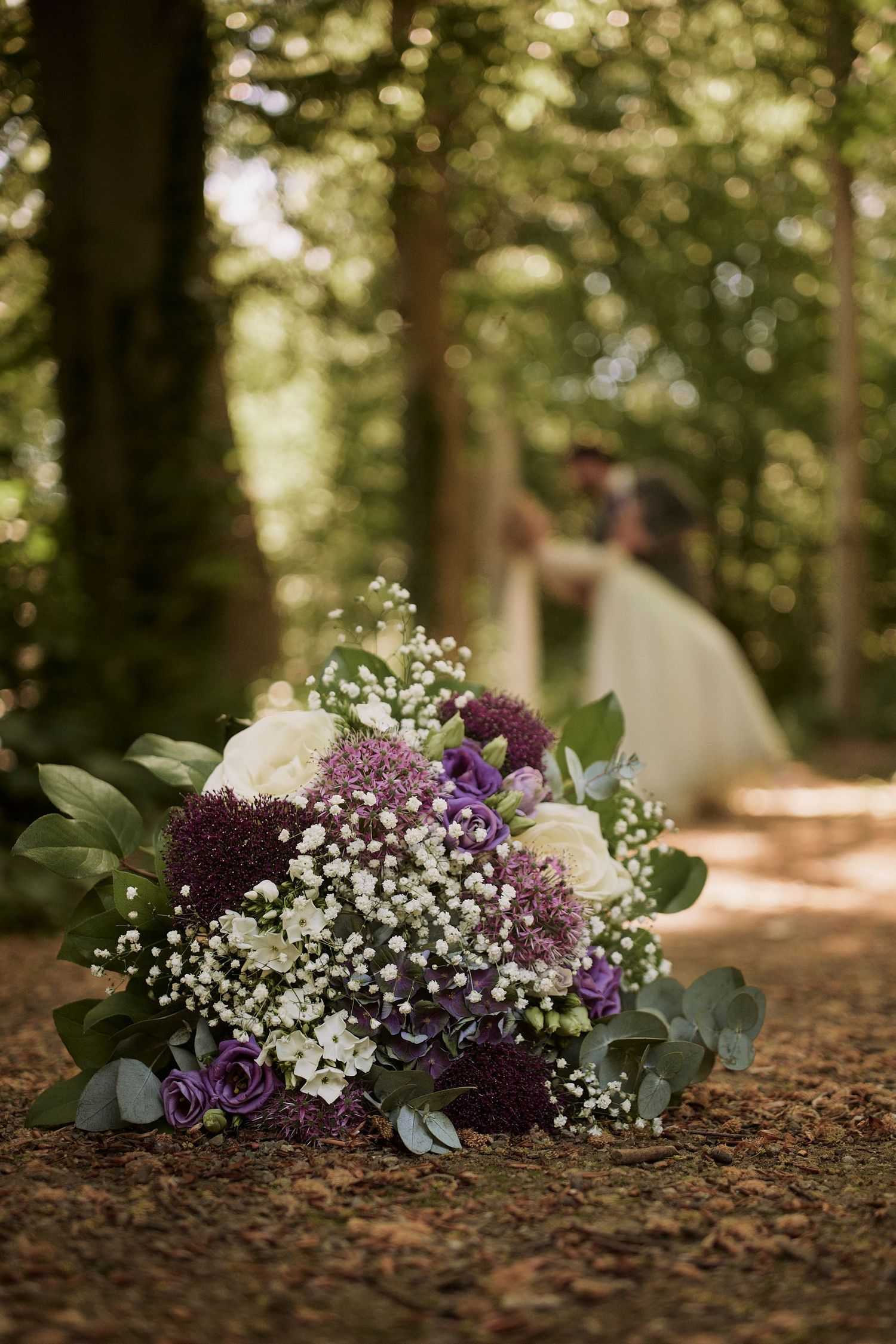 A beautiful wedding bouquet with purple flowers and baby's breath on a forest path.