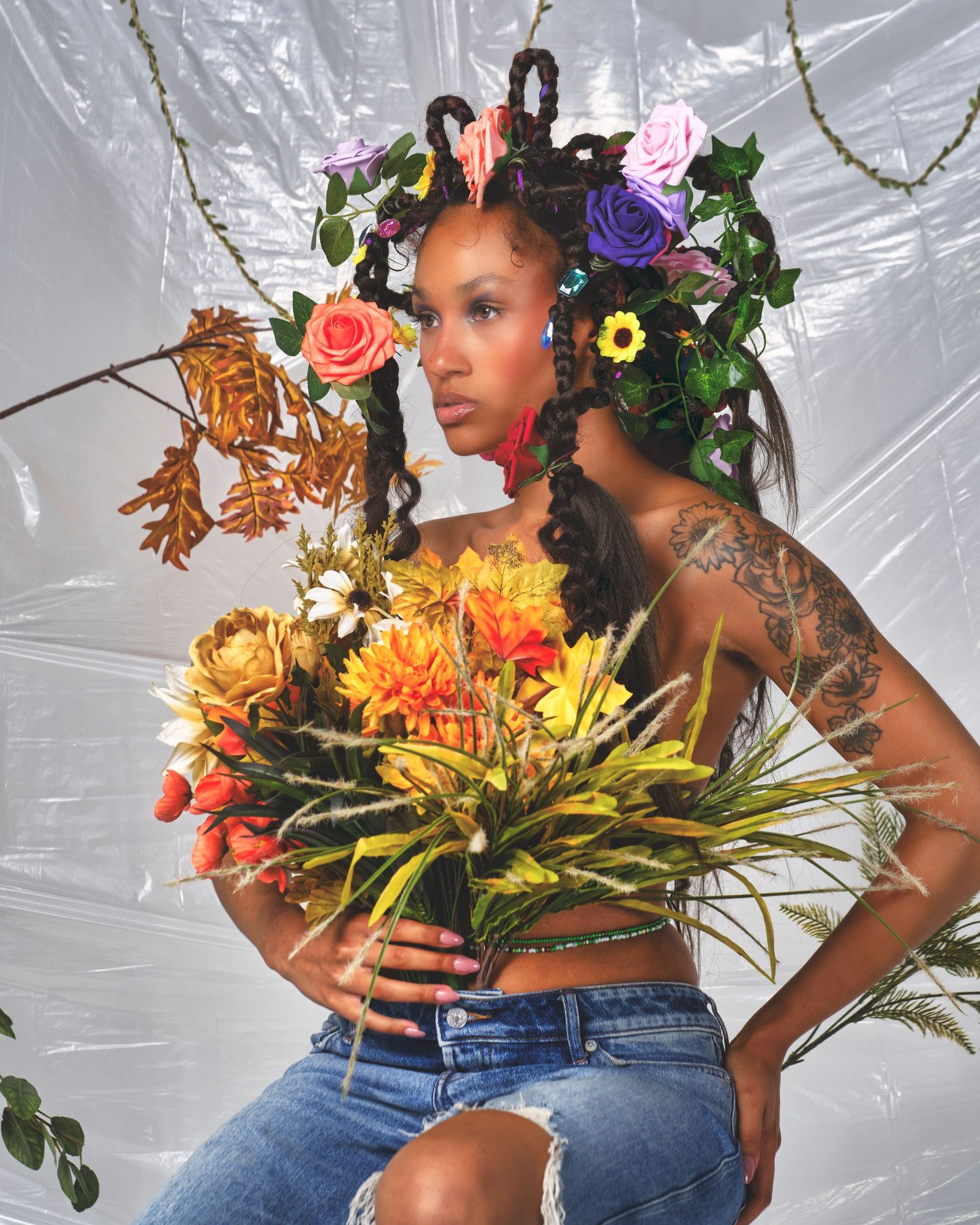Creative portrait with colorful flowers and foliage arranged as hair accessories against white backdrop.