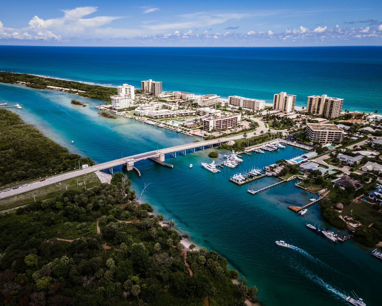 Aerial panoramic view of Jupiter Inlet in Florida showing boats, marina, waterways and coastal buildings against blue water.