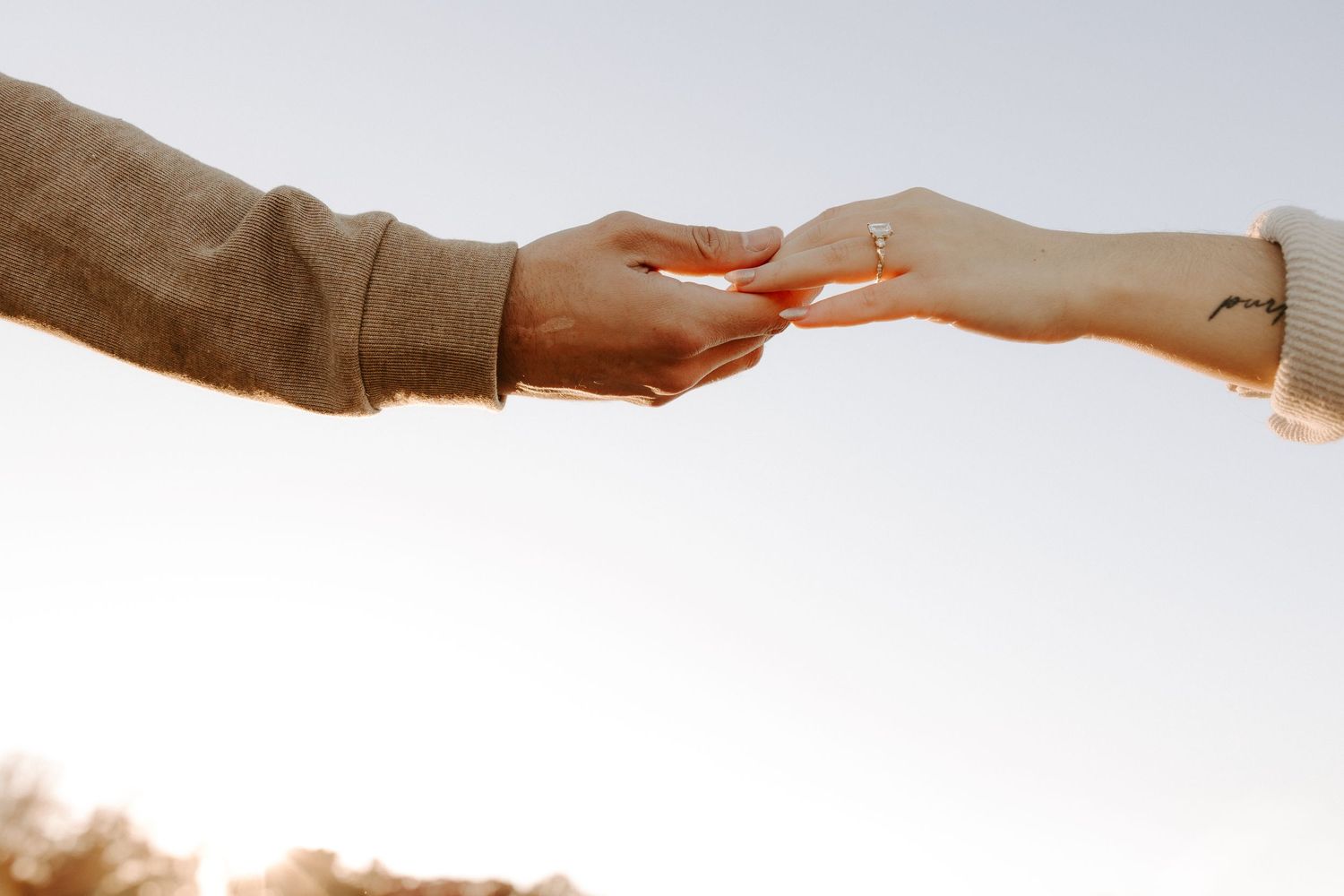 Two hands reaching toward each other against a bright sky background.