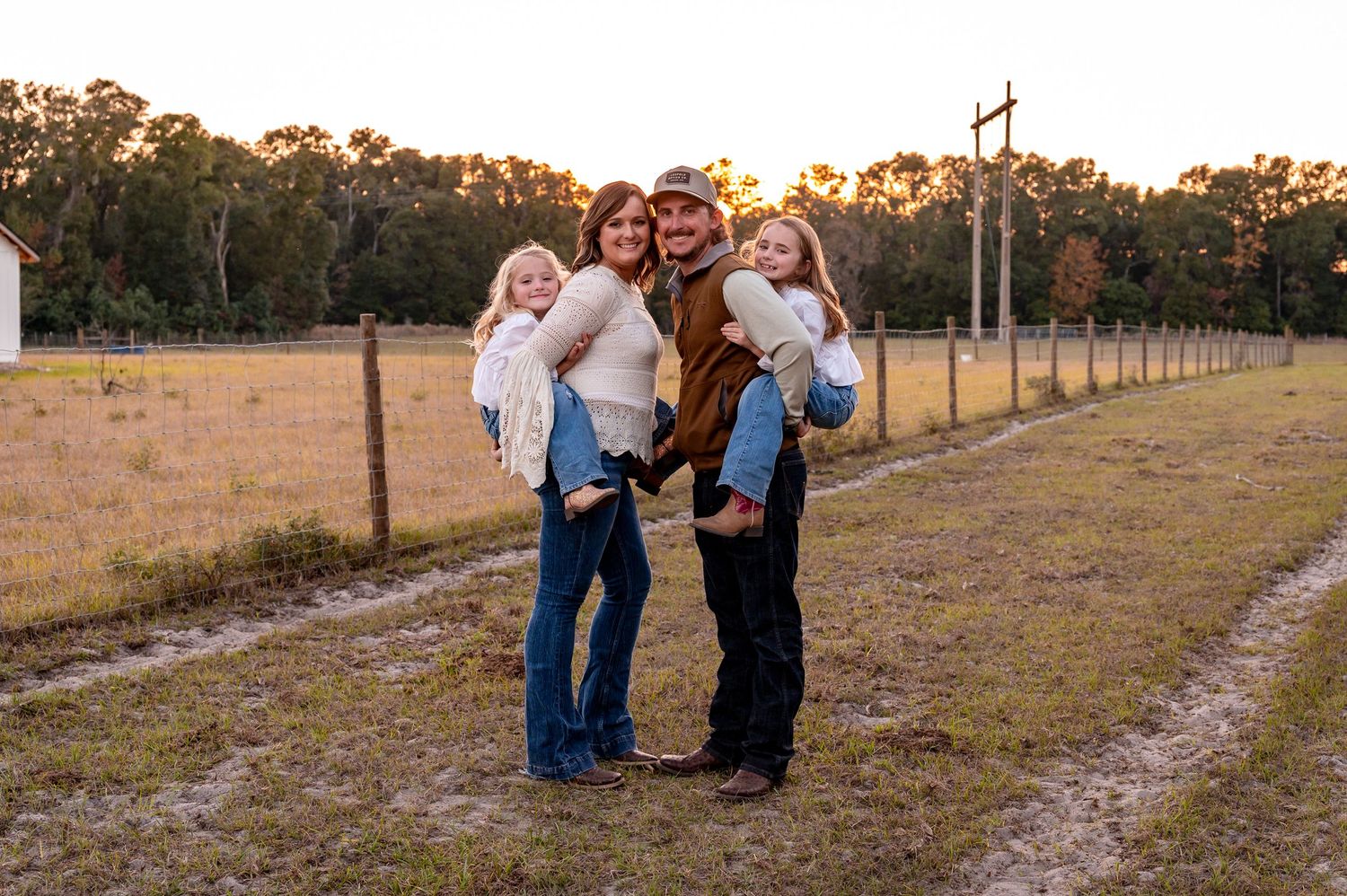 A family walks together through a golden field at sunset, casting long shadows across the grass.