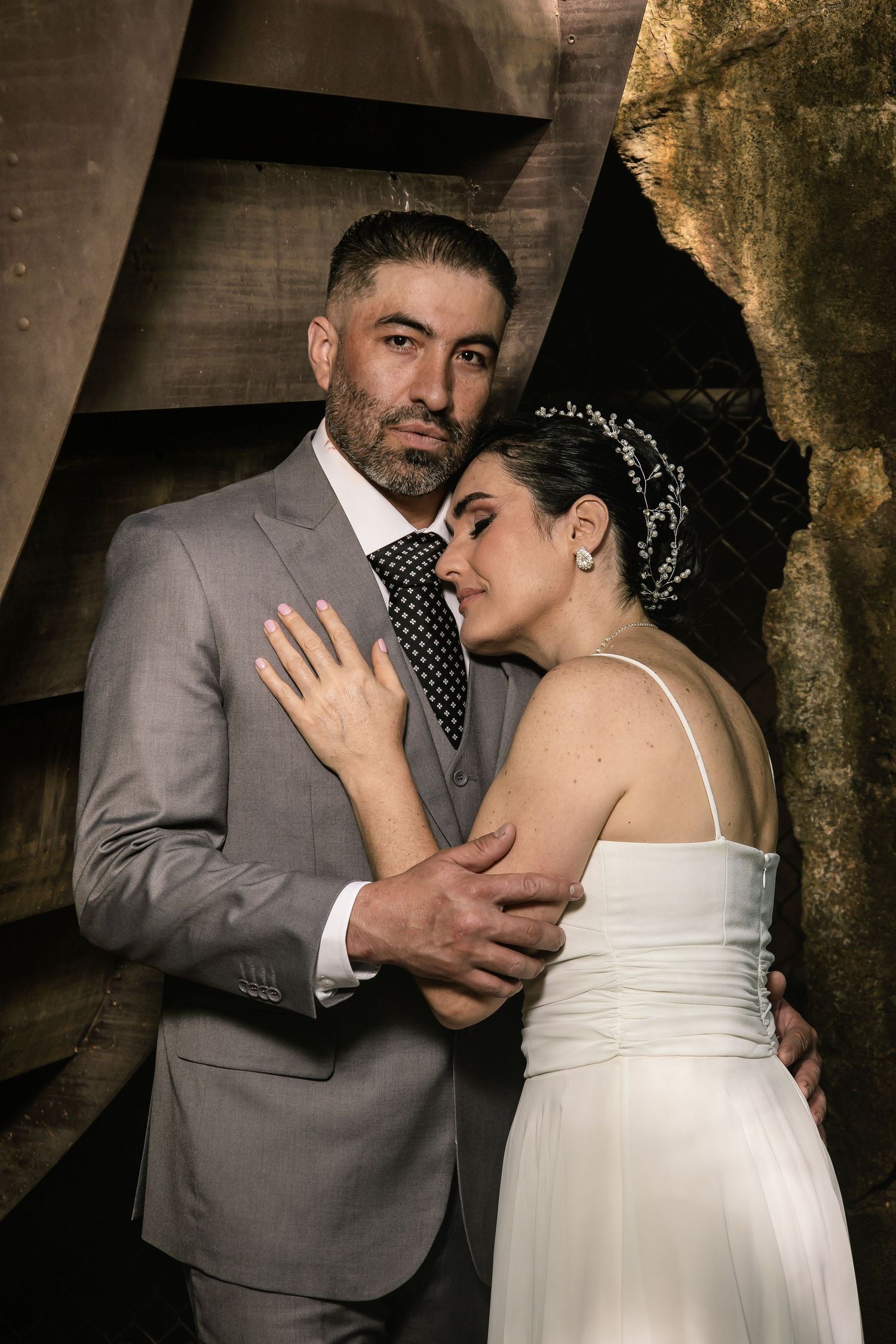 Intimate wedding portraits of couple in formal attire against textured wall.