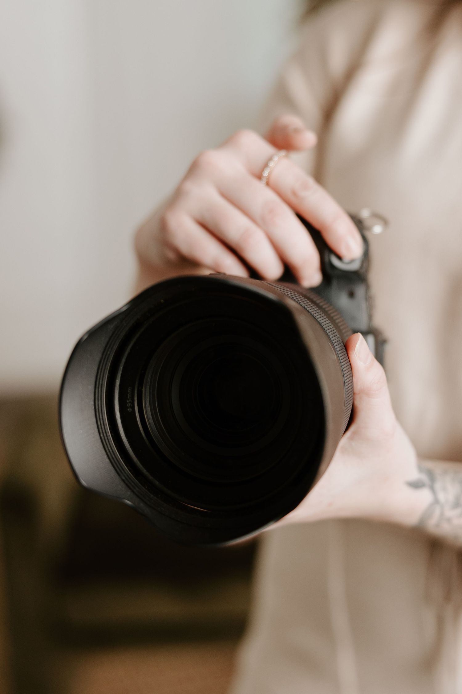 Close-up view of hands holding a professional camera lens against a neutral background.