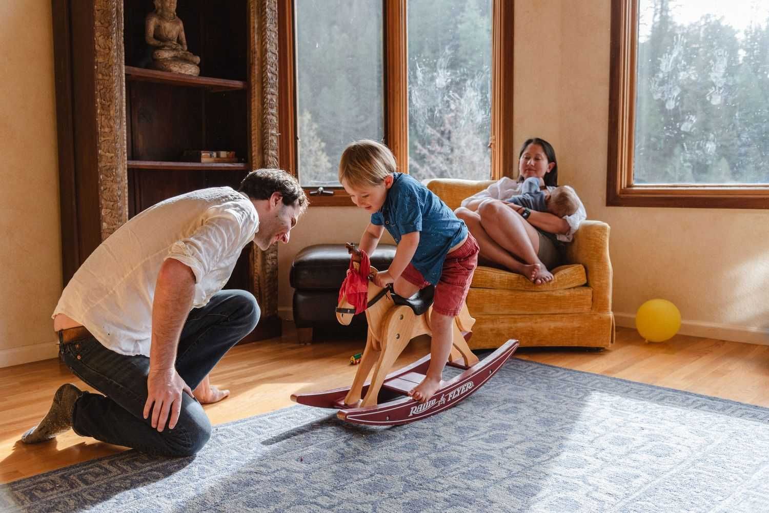 Family playtime indoors with a rocking toy on a gray rug.