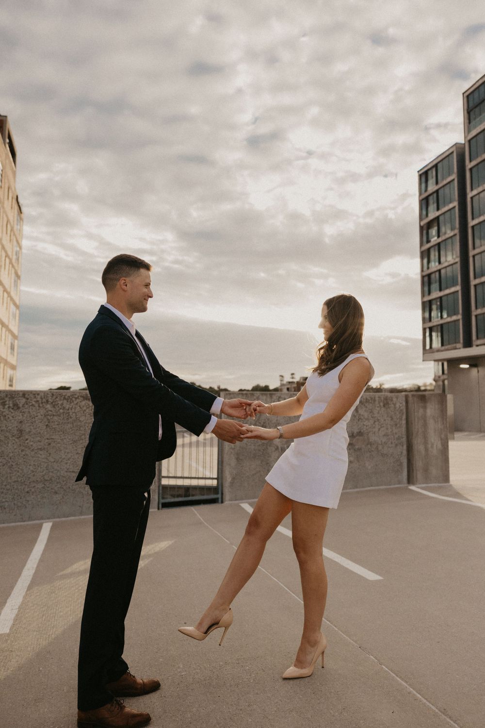 Couple dancing together on rooftop parking area with city buildings behind them.