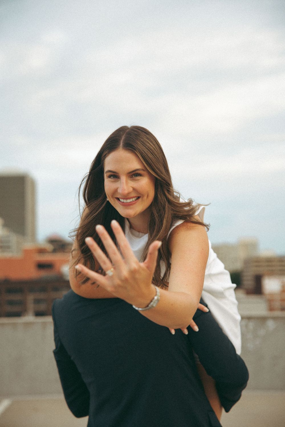 Person in white top smiling while being lifted on urban rooftop.
