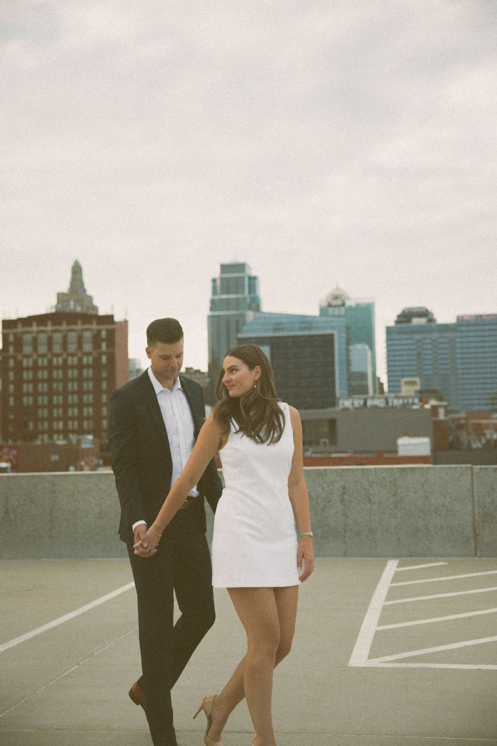A couple shares a romantic moment on a rooftop with the city skyline behind them.