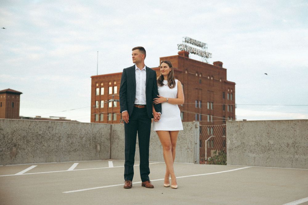 A couple poses together on an urban rooftop with historic brick buildings in the background.