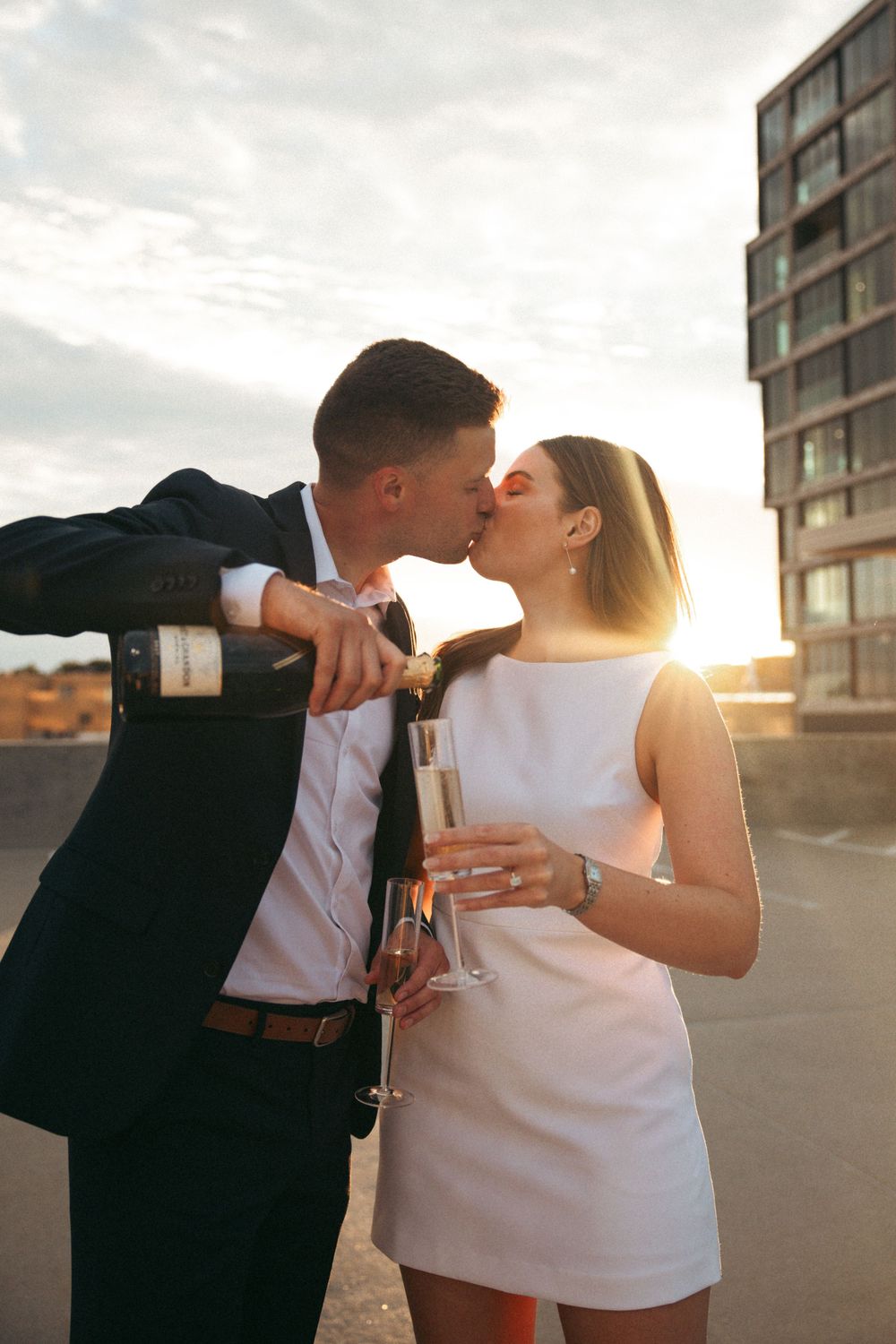 A couple shares an intimate moment with champagne at sunset on a rooftop.
