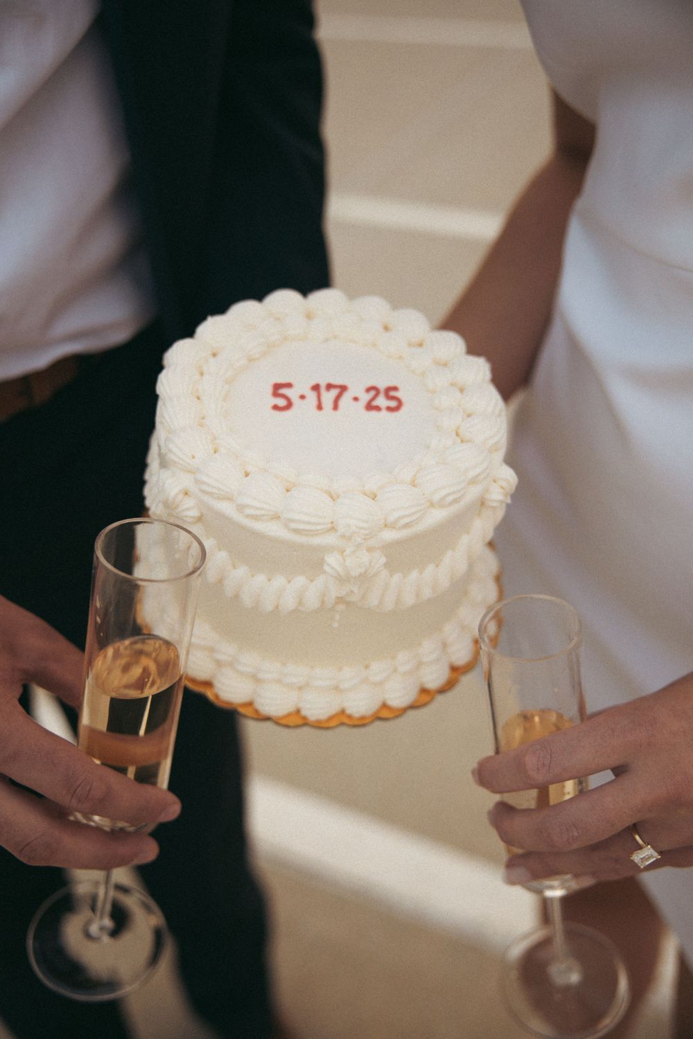 A white wedding cake with the date 5-17-25 and champagne glasses.