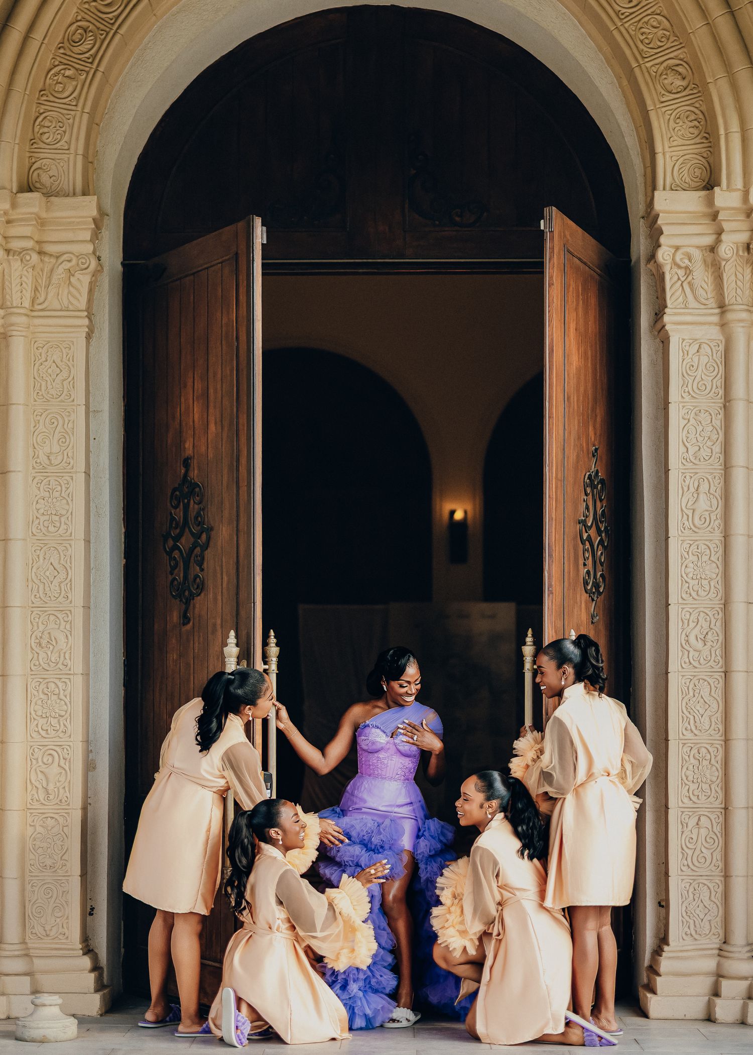 Wedding party wearing vibrant red dresses and yellow accessories poses together with bride in yellow and pink gown.