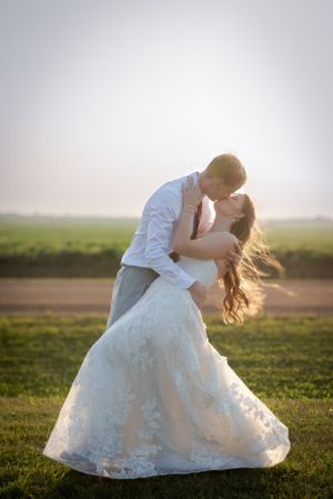 A portrait of a groom dipping a bride at sunset and kissing.