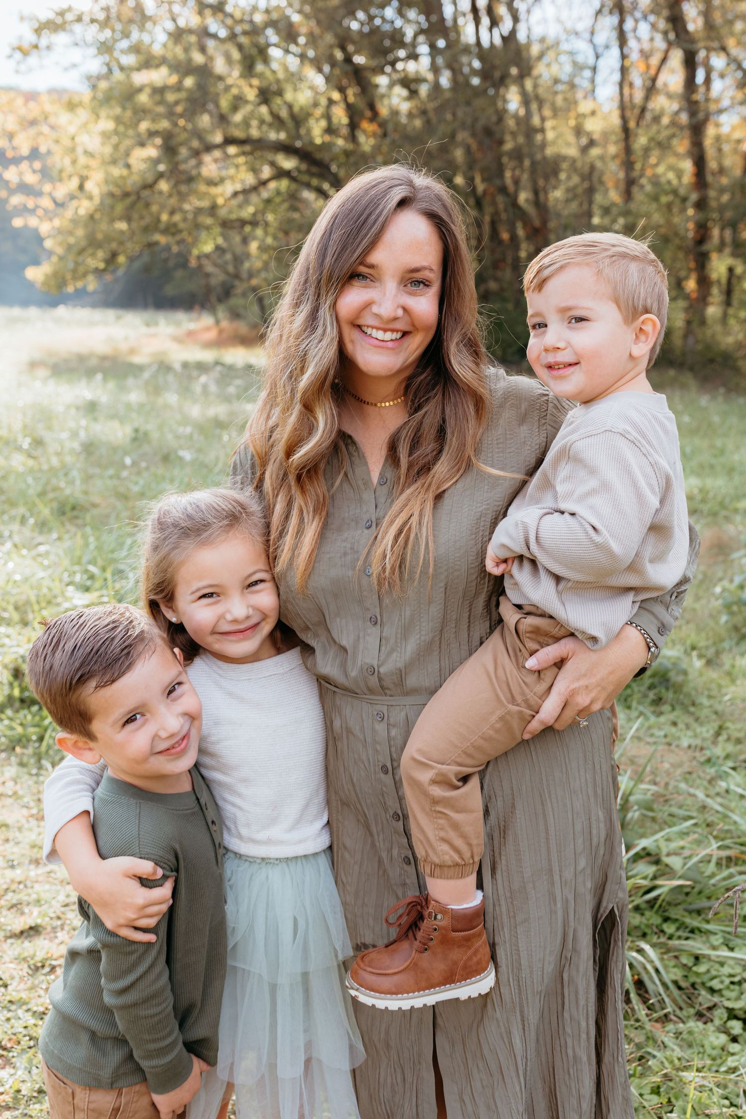 Family of four posing together in grassy field at sunset.
