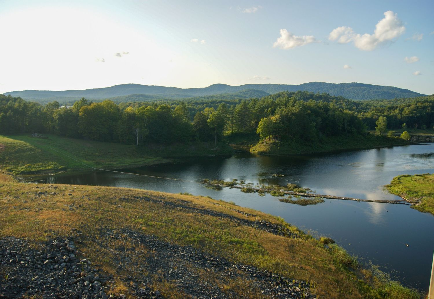 Scenic mountain lake view with green forest and blue water under a partly cloudy sky.