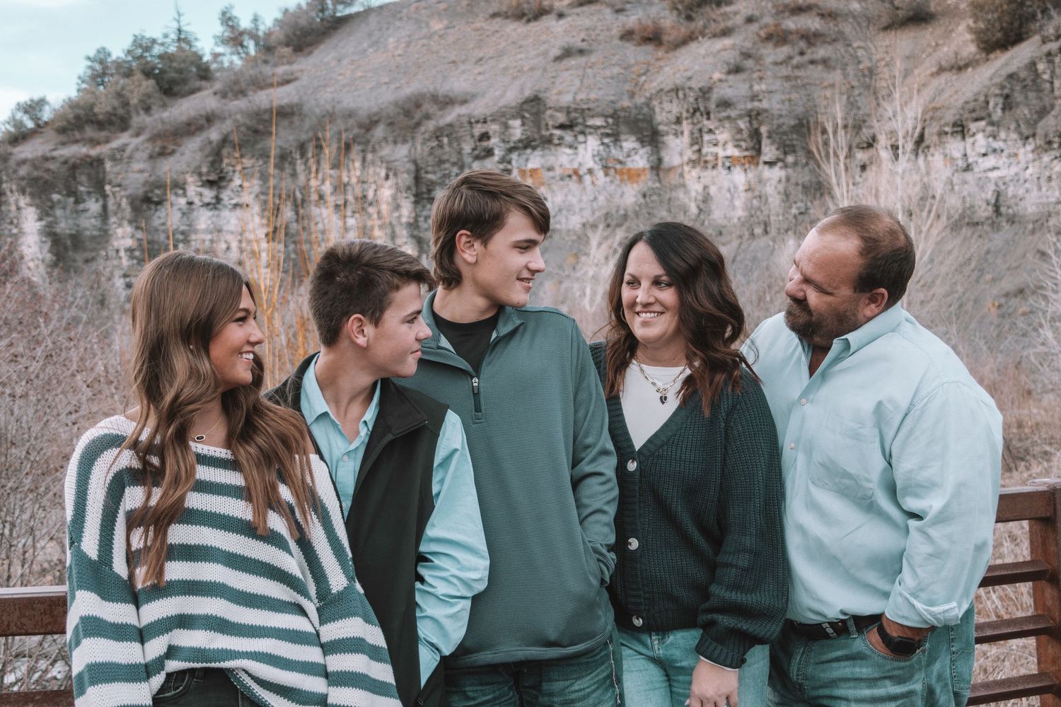 Family poses casually together on metal bench against limestone cliff backdrop.