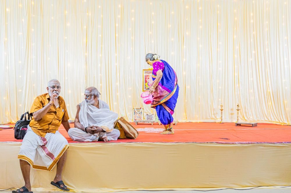 People sitting on a decorated stage during a traditional Indian cultural event.