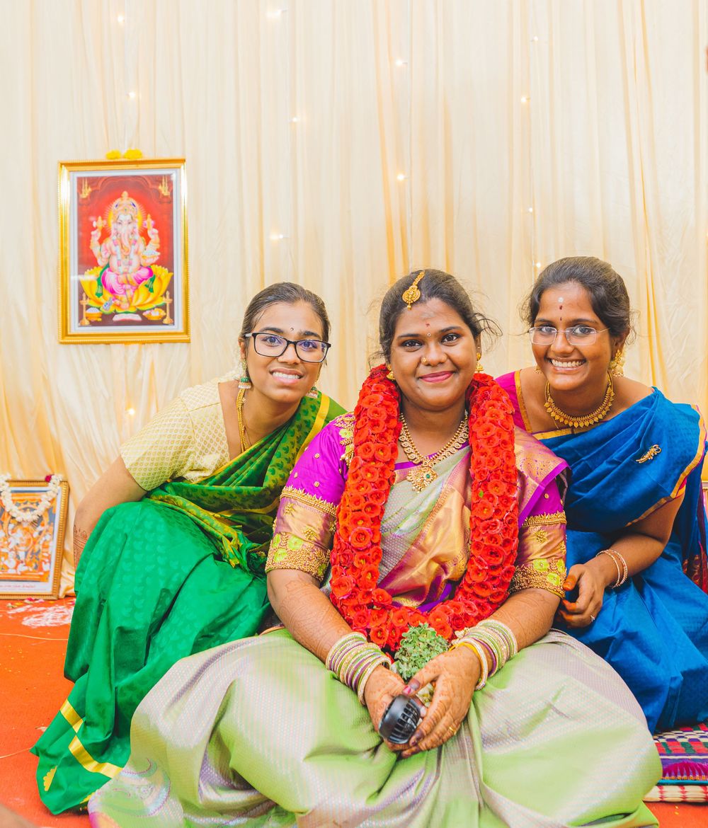 Three women in colorful traditional Indian sarees sit together smiling with a Ganesh portrait on the wall.