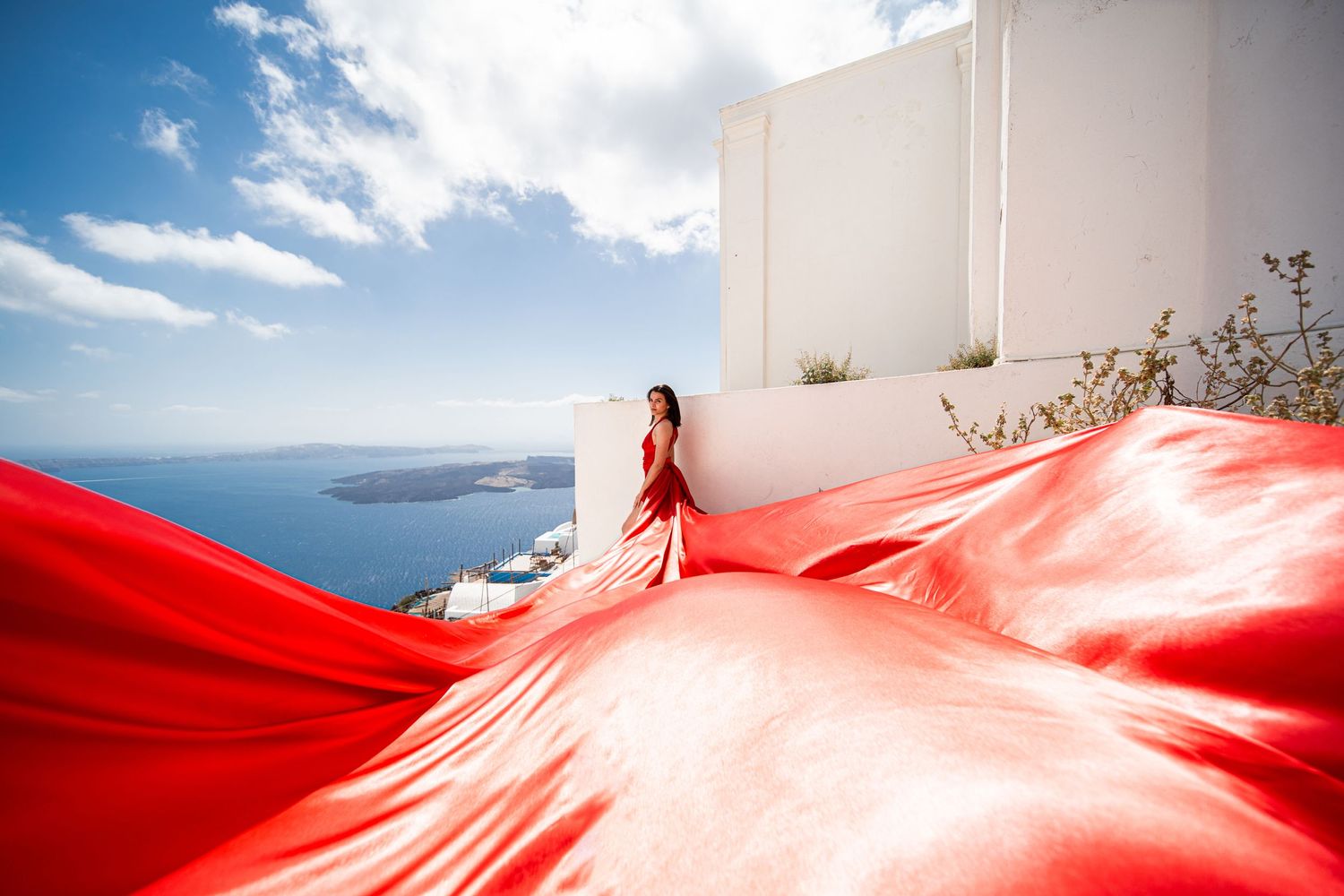 Stunning red flowing dress contrasts with white architecture and sea views in Santorini.