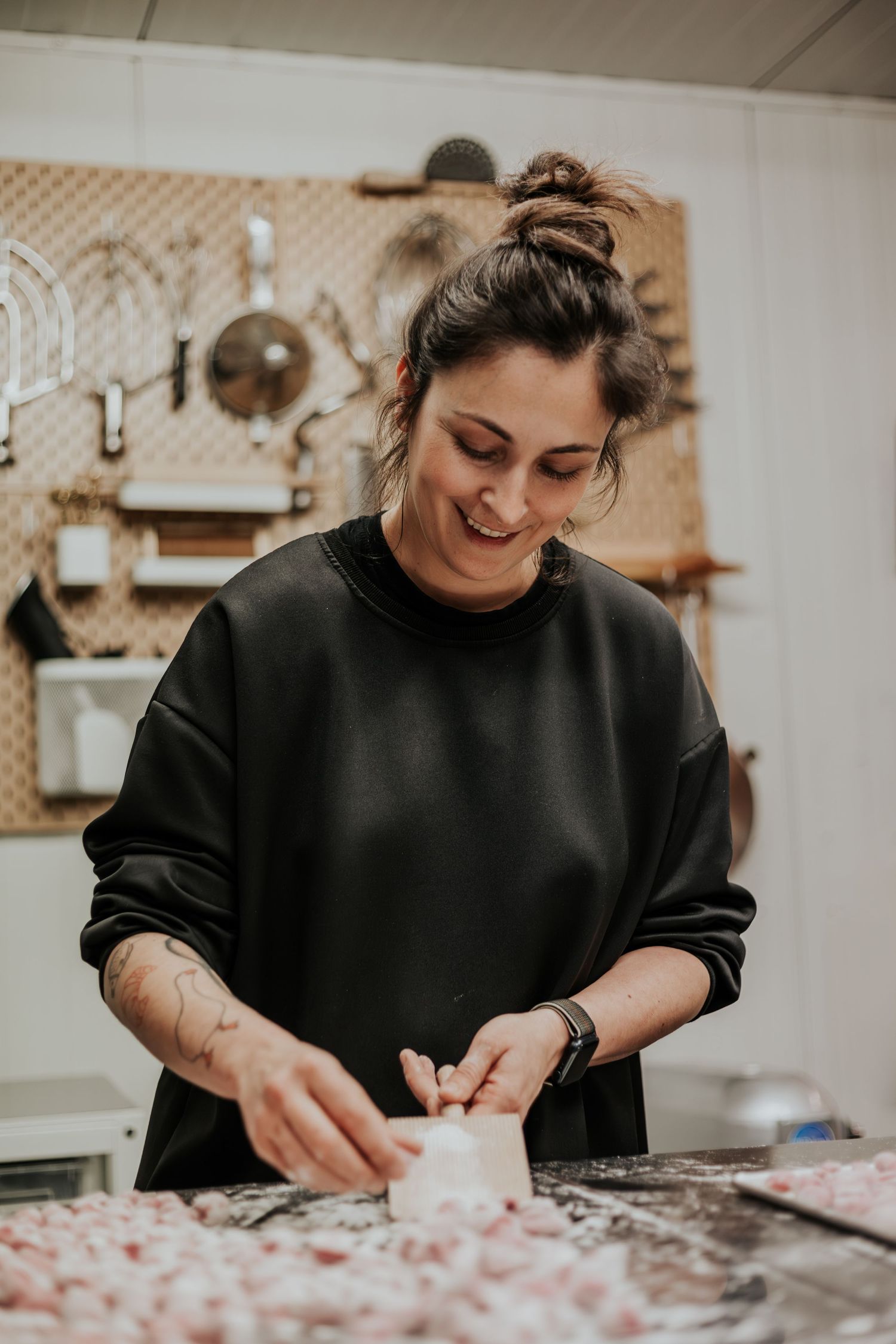 Person in black sweater working with dough and flour on a kitchen counter while smiling and preparing food.