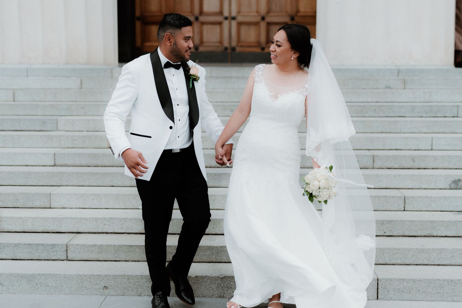 A couple sitting on white marble steps sharing a romantic moment in their wedding attire.