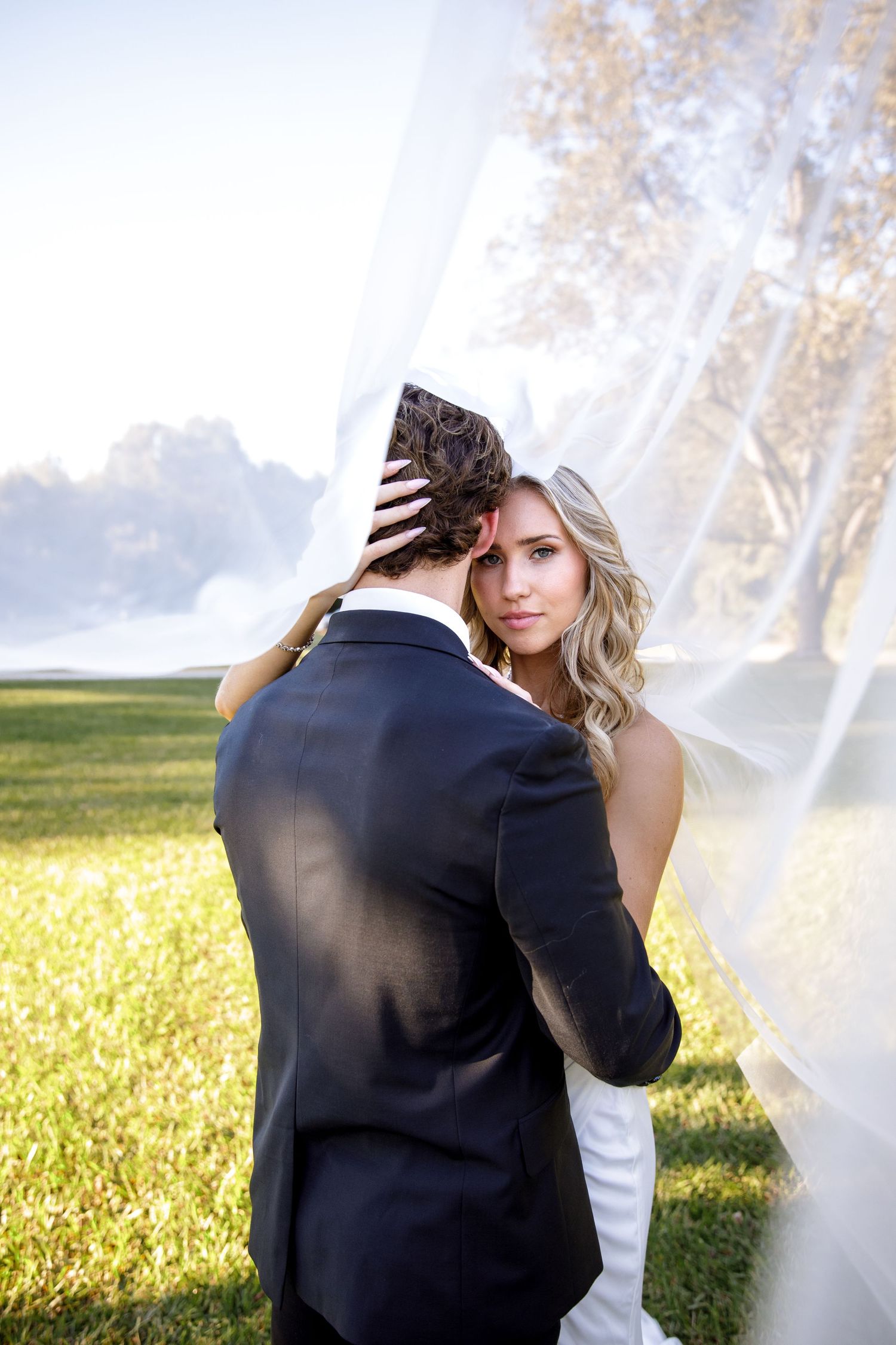 Romantic wedding photos in a sunlit field with flowing veil.
