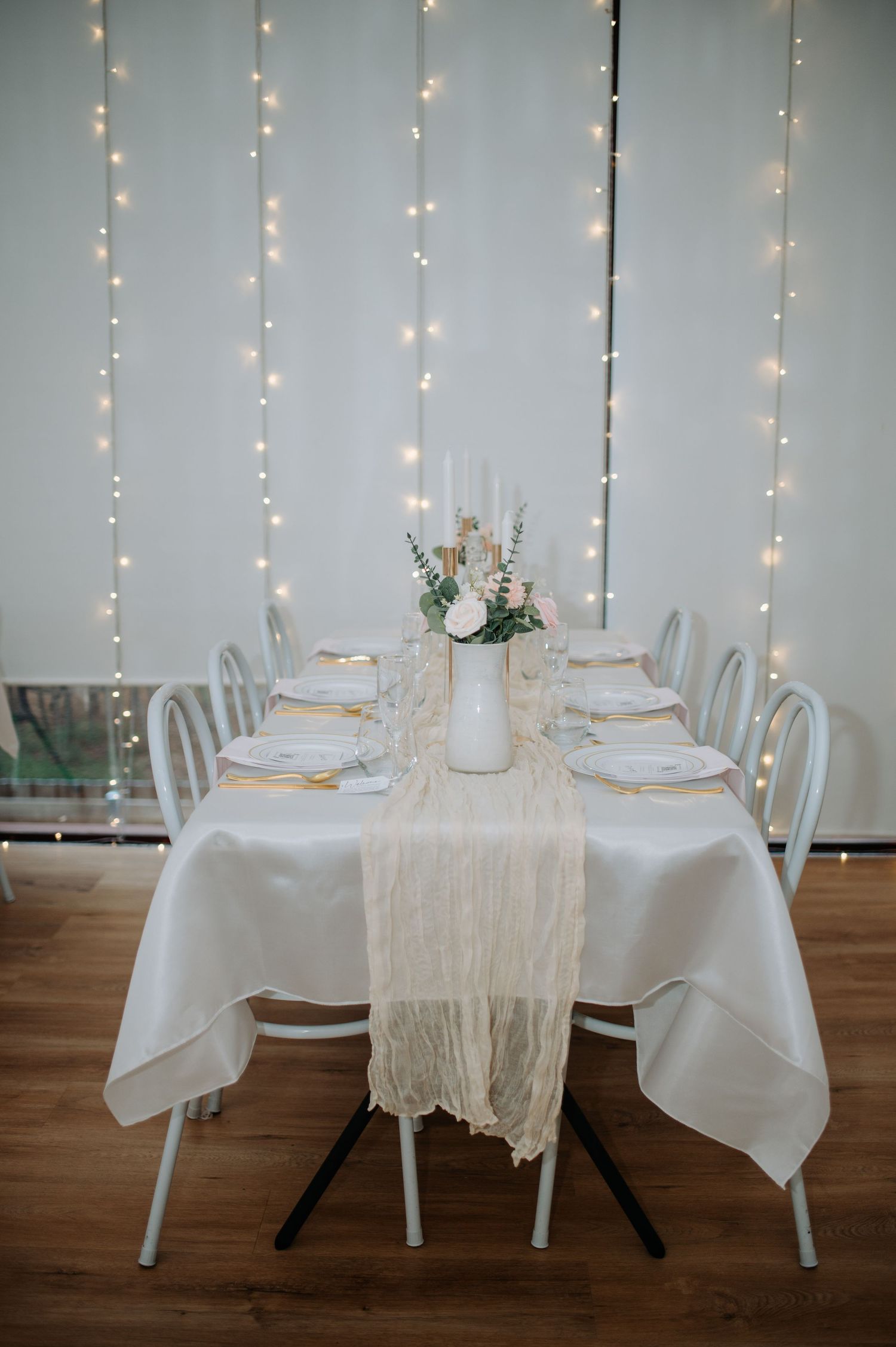 Romantic wedding reception table with fairy lights, white linens and floral centerpiece.