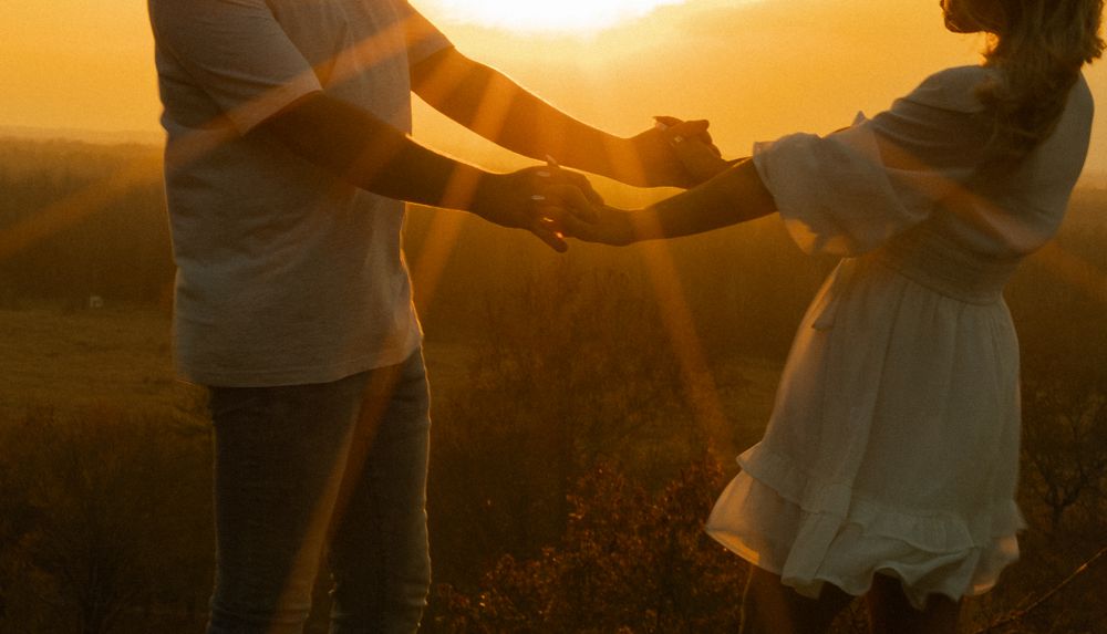 Two people hold hands silhouetted against a dramatic sunset.