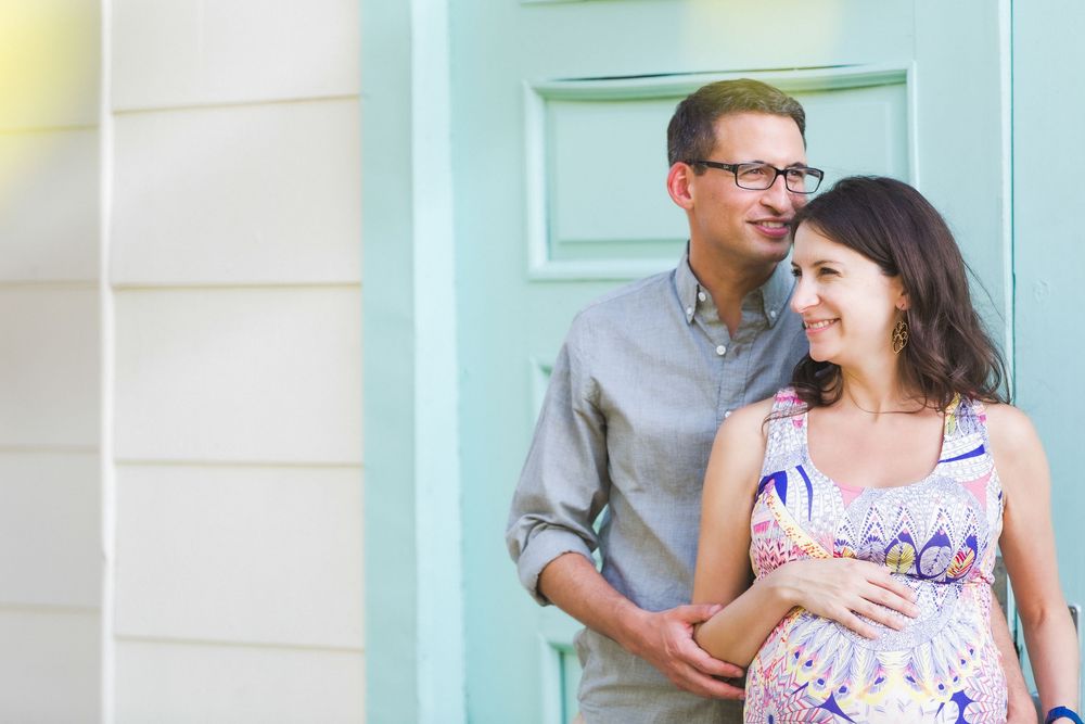 A couple in casual attire shares intimate moments while posing against a light colored wall.