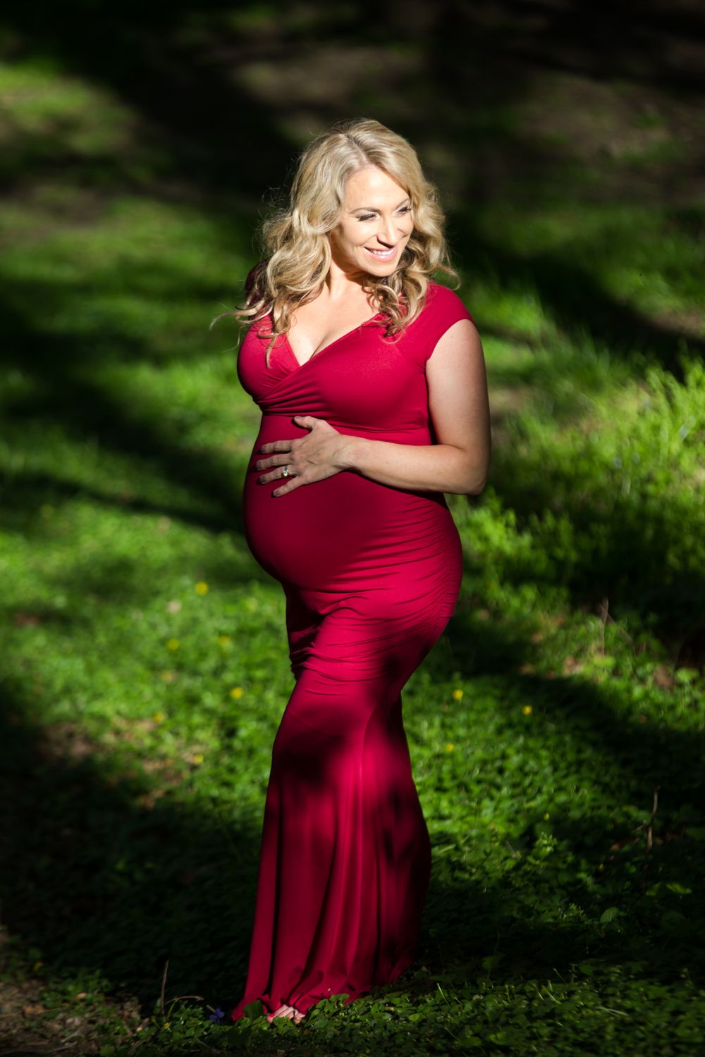 Outdoor maternity photos in a red dress amid lush greenery and natural lighting.