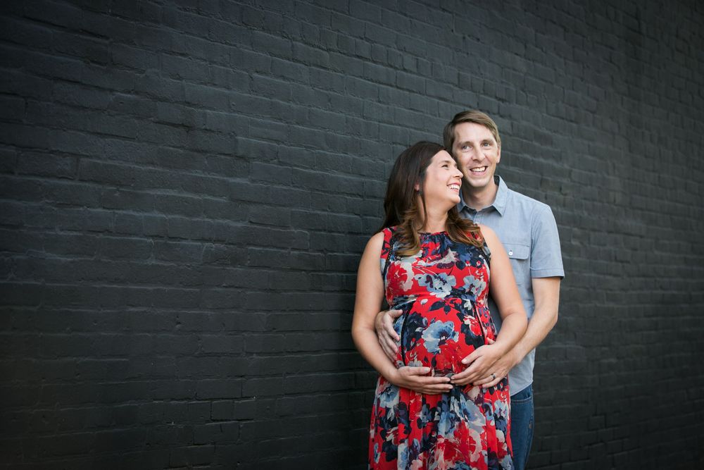 A romantic couple embraces against a dark brick wall background.
