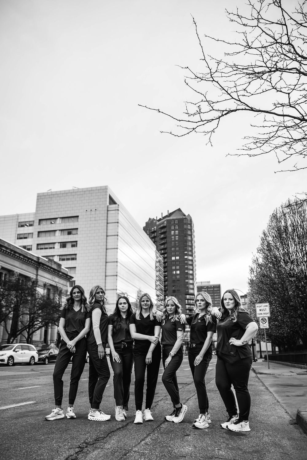 Black and white photo of a group posing casually on an urban sidewalk with city buildings in the background.
