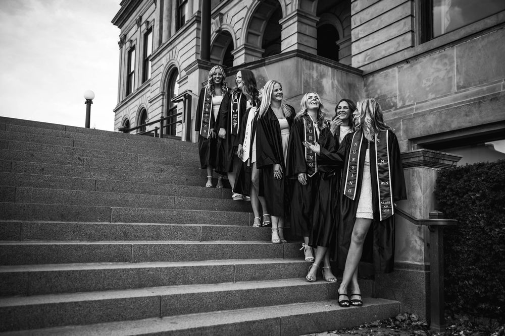 A black and white photo shows graduates in caps and gowns descending stone steps of a grand building.