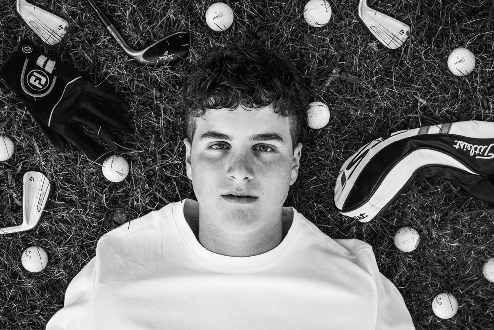 Overhead view of golf equipment arranged around figure lying on grass.