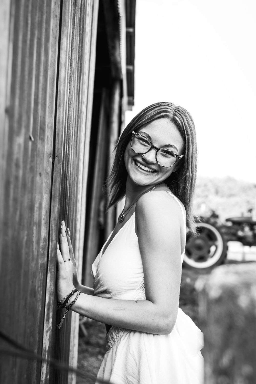 Black and white portrait by wooden barn door showing joyful expression.